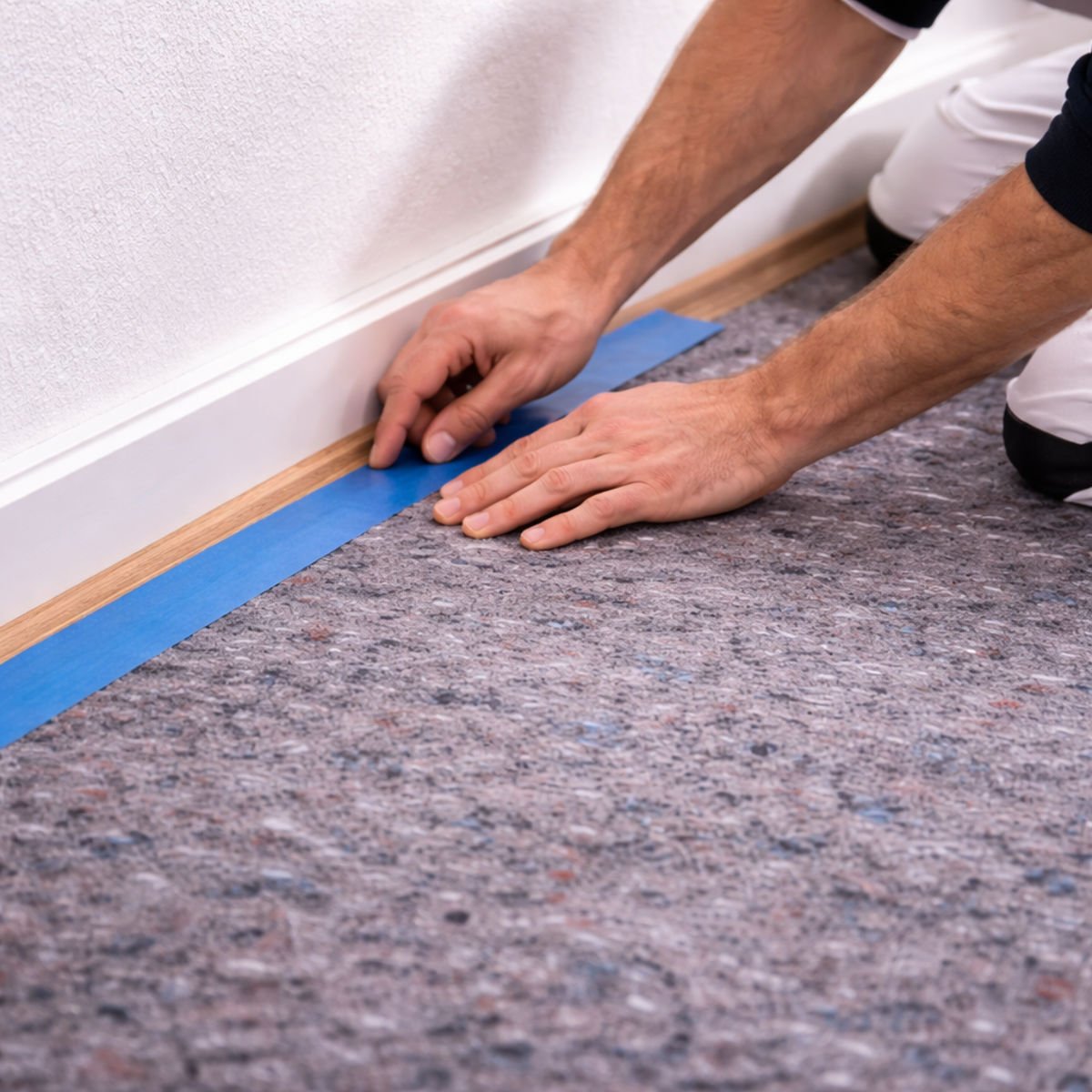 Maler fixiert Abdeckvlies mit Klebeband an Sockelleiste – sauberer Kantenschutz beim Streichen